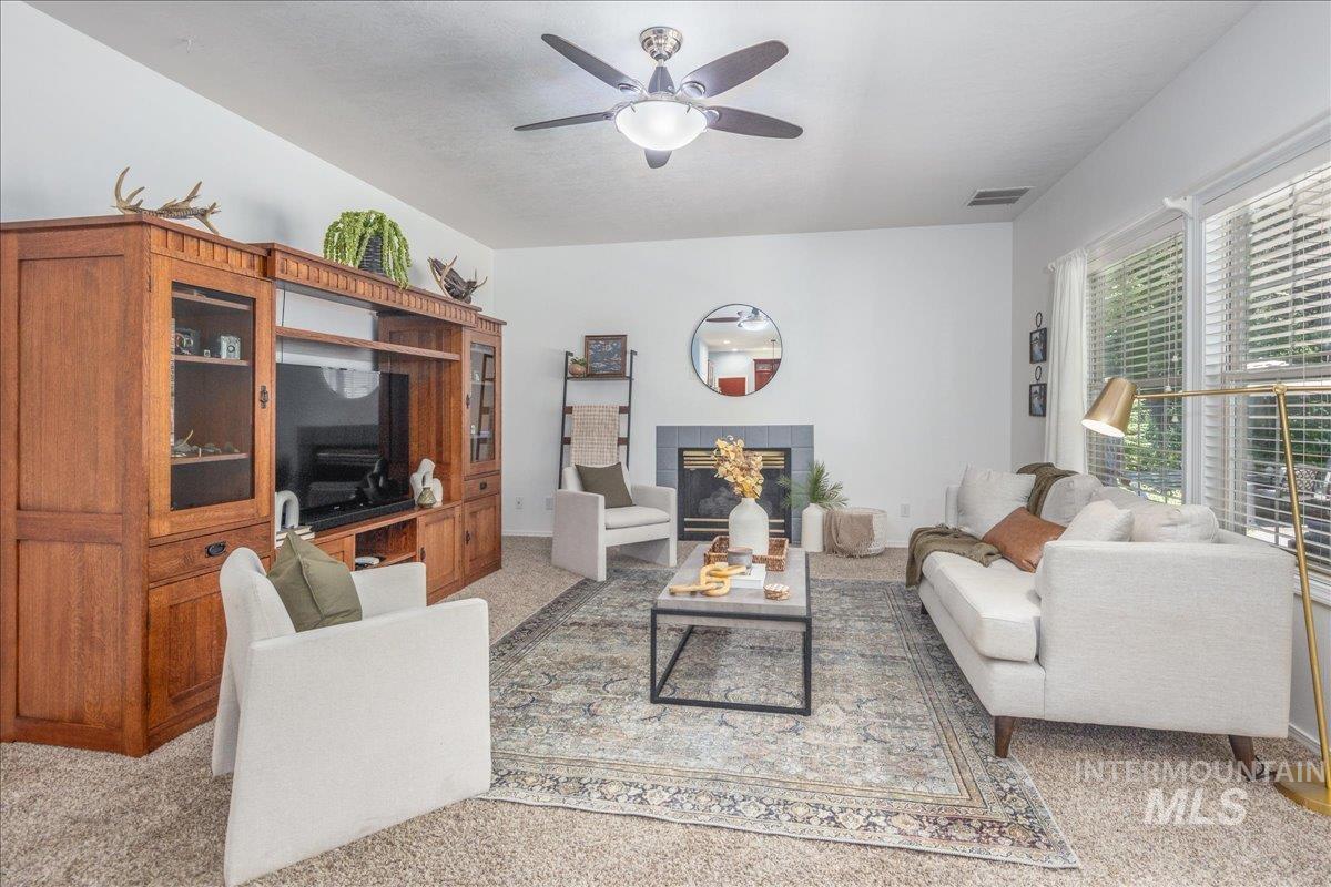 Living room featuring ceiling fan, light carpet, and a tiled fireplace