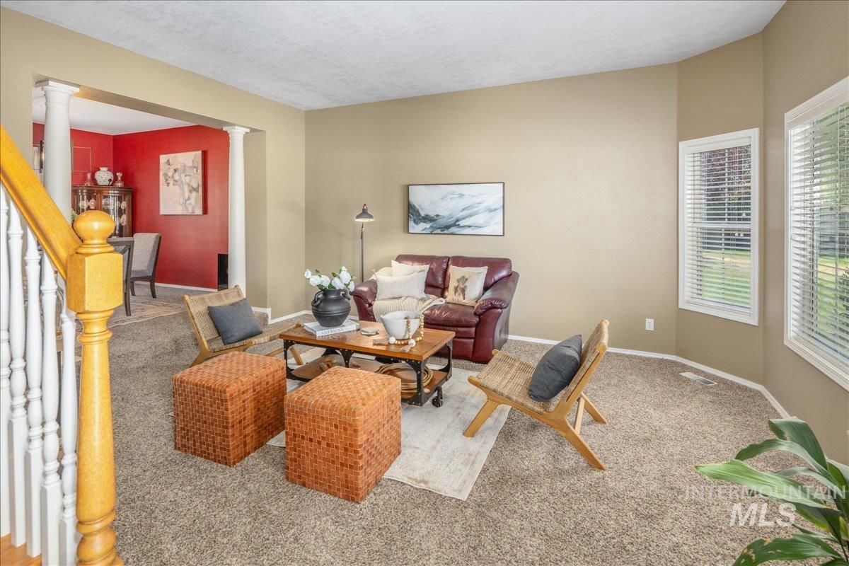 Carpeted living room featuring decorative columns and baseboards