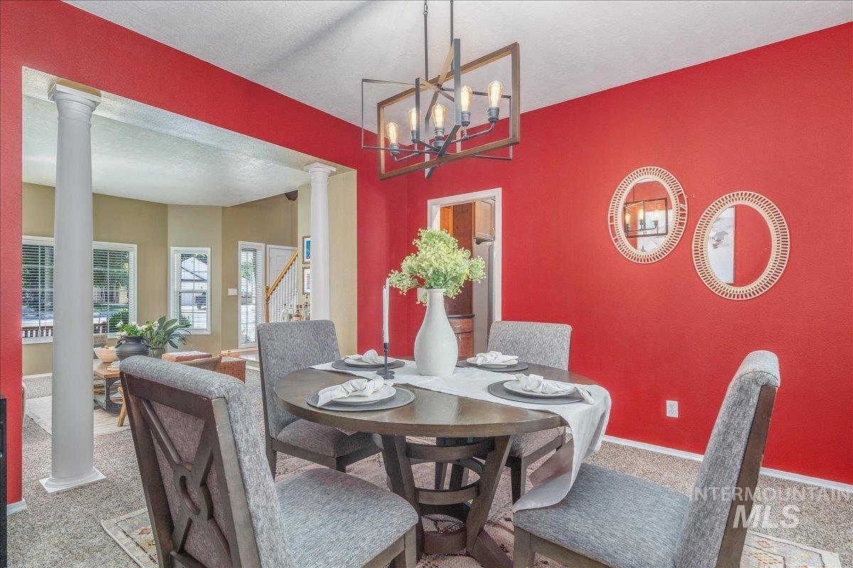 Carpeted dining room featuring decorative columns, stairway, and a chandelier