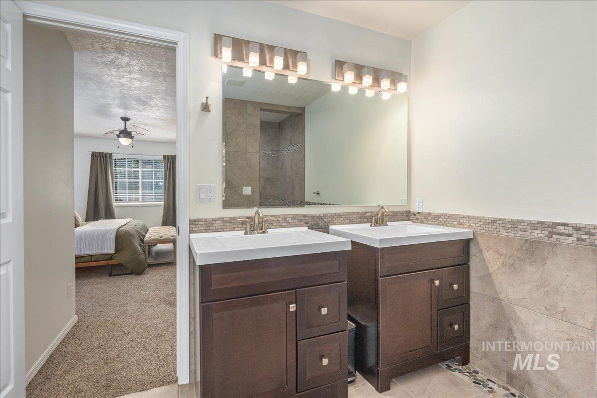 Bathroom with two vanities, tile walls, ensuite bath, and a ceiling fan