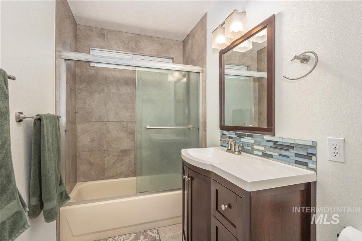 Bathroom with vanity, bath / shower combo with glass door, and tasteful backsplash