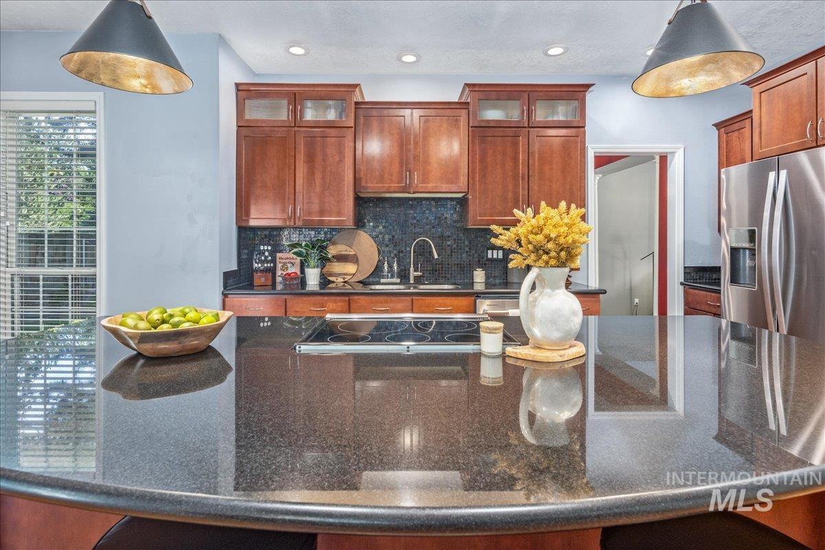 Kitchen with stainless steel fridge with ice dispenser, decorative backsplash, glass insert cabinets, dark stone countertops, and recessed lighting