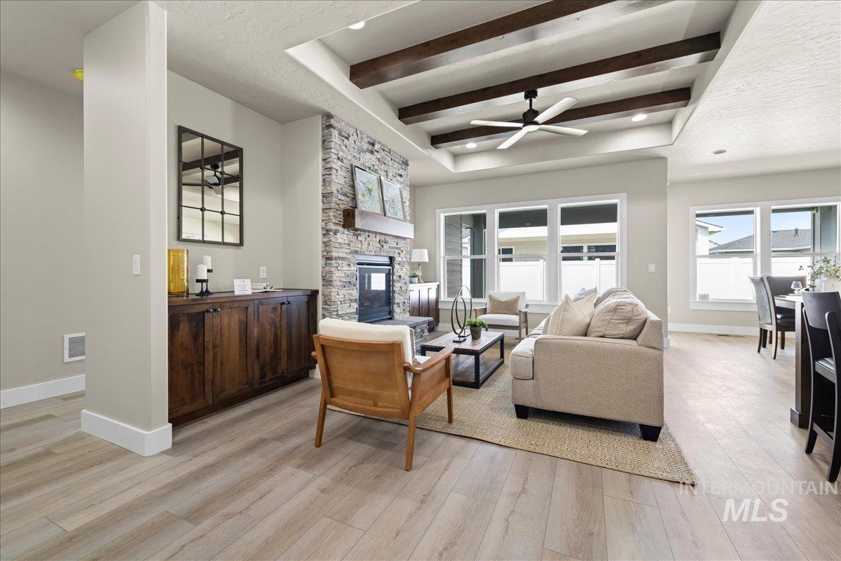 Living area featuring a fireplace, ceiling fan, beam ceiling, light wood-style flooring, and a raised ceiling