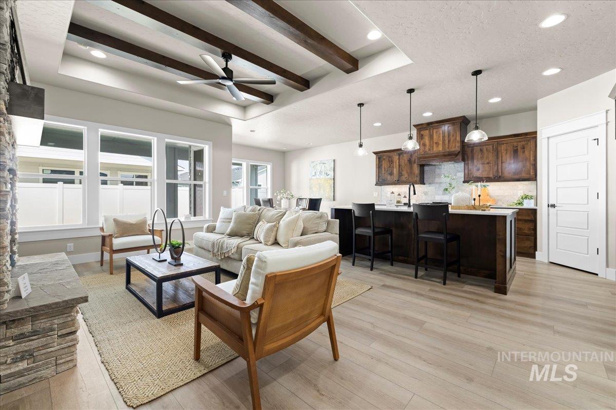 Living room featuring beam ceiling, light wood-type flooring, a ceiling fan, a tray ceiling, and recessed lighting