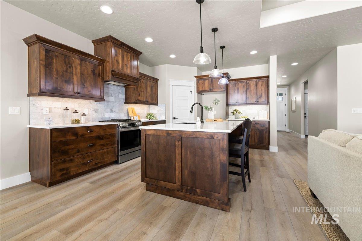 Kitchen featuring tasteful backsplash, stainless steel gas stove, hanging light fixtures, a textured ceiling, and dark brown cabinets