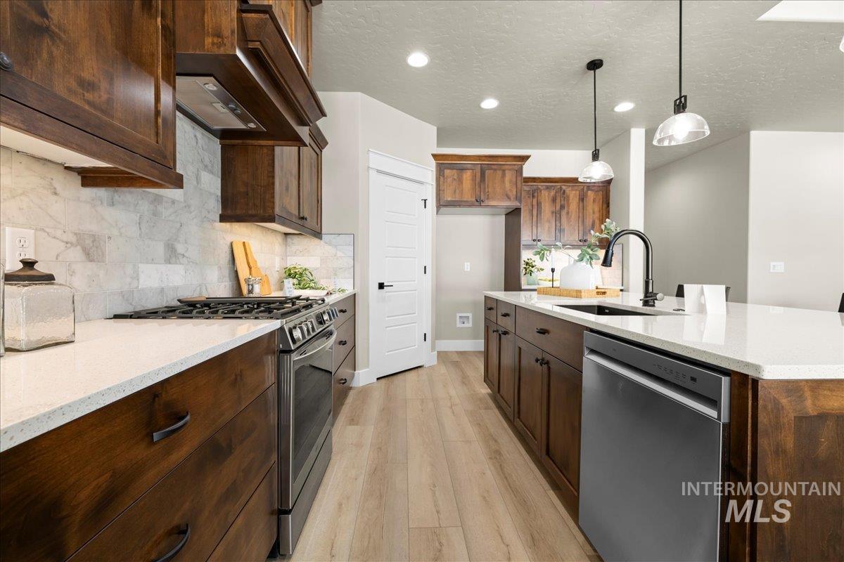 Kitchen with stainless steel appliances, light stone counters, light wood-style flooring, a textured ceiling, and decorative light fixtures