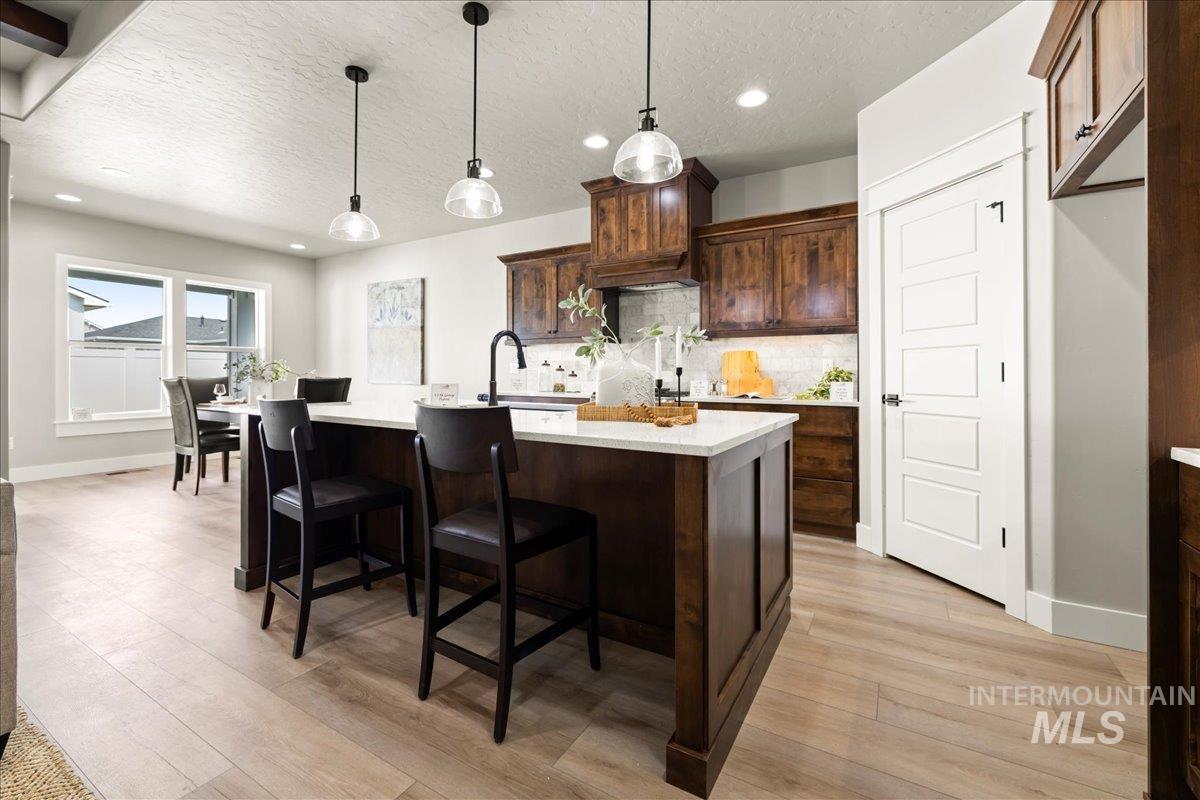 Kitchen with tasteful backsplash, decorative light fixtures, an island with sink, a textured ceiling, and dark brown cabinetry