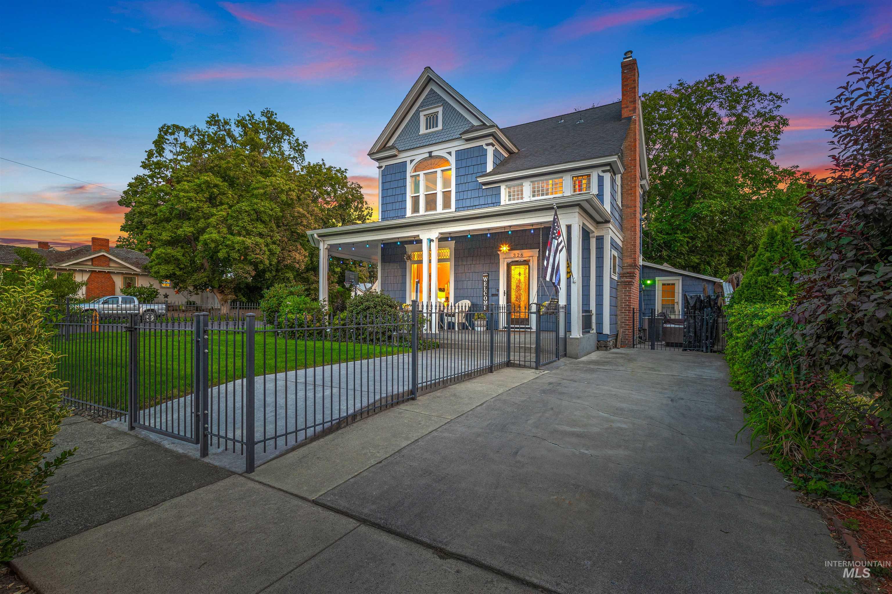 View of front of property with a gate, a chimney, a fenced front yard, concrete driveway, and covered porch