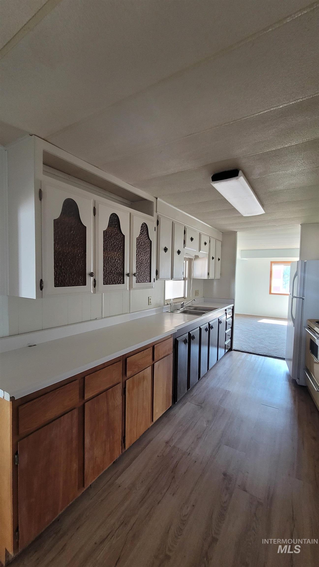 Kitchen with light countertops, brown cabinetry, white cabinetry, dark wood finished floors, and appliances with stainless steel finishes