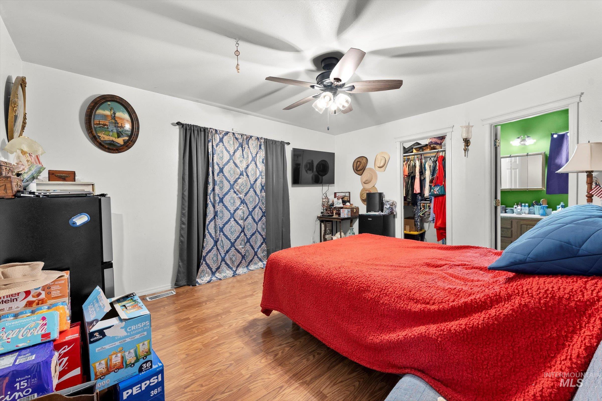 Bedroom with light wood-style floors, freestanding refrigerator, a walk in closet, a ceiling fan, and ensuite bath