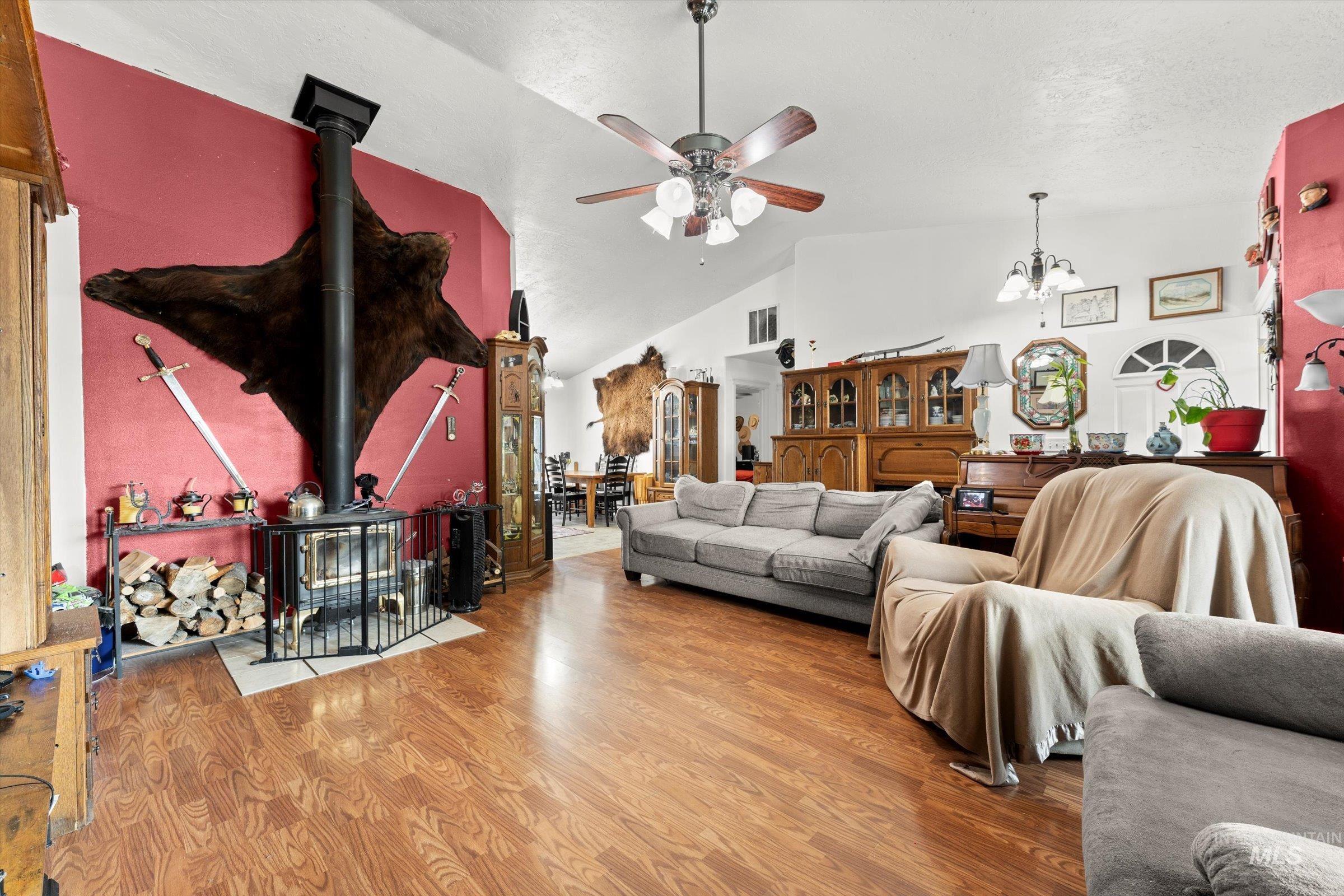 Living room with a wood stove, wood finished floors, vaulted ceiling, a chandelier, and a ceiling fan