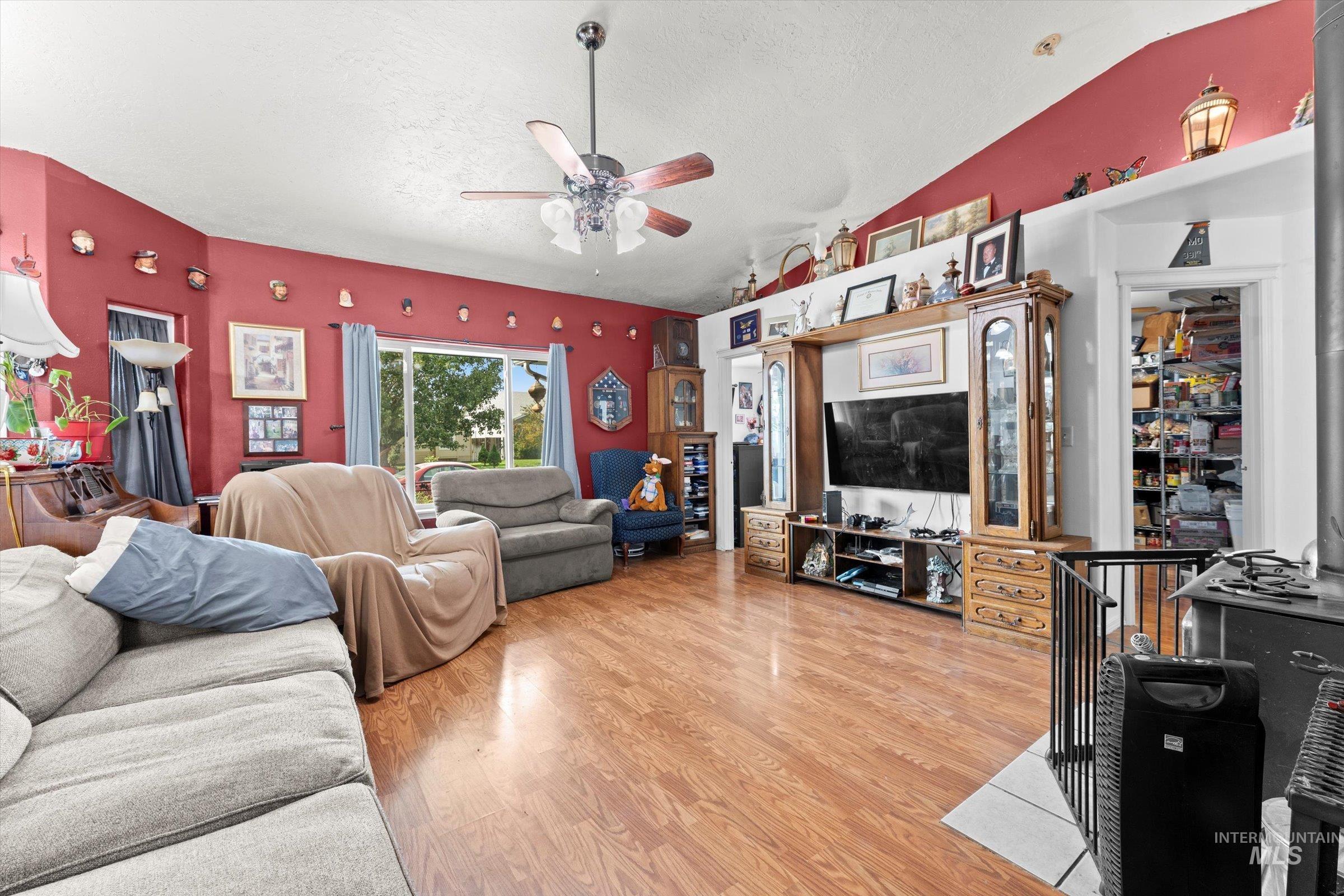 Living area with ceiling fan, light wood-style flooring, a textured ceiling, and lofted ceiling