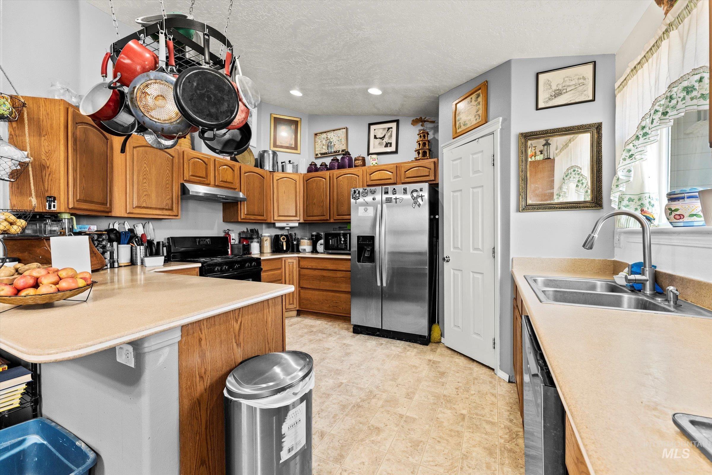 Kitchen featuring appliances with stainless steel finishes, brown cabinets, light countertops, a peninsula, and a textured ceiling