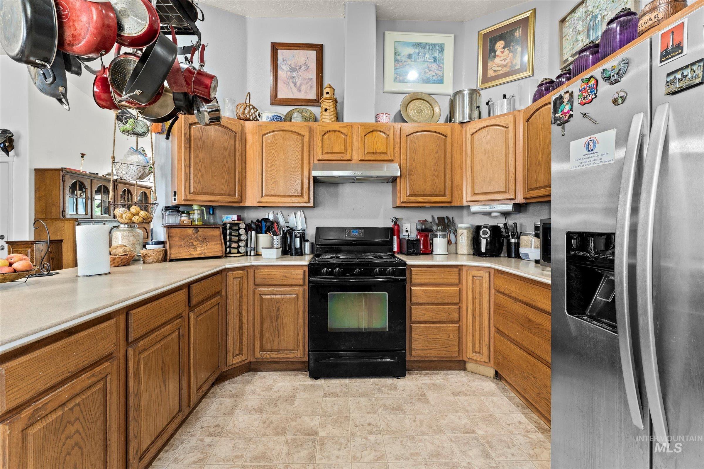 Kitchen featuring stainless steel fridge with ice dispenser, black gas stove, light countertops, and brown cabinetry