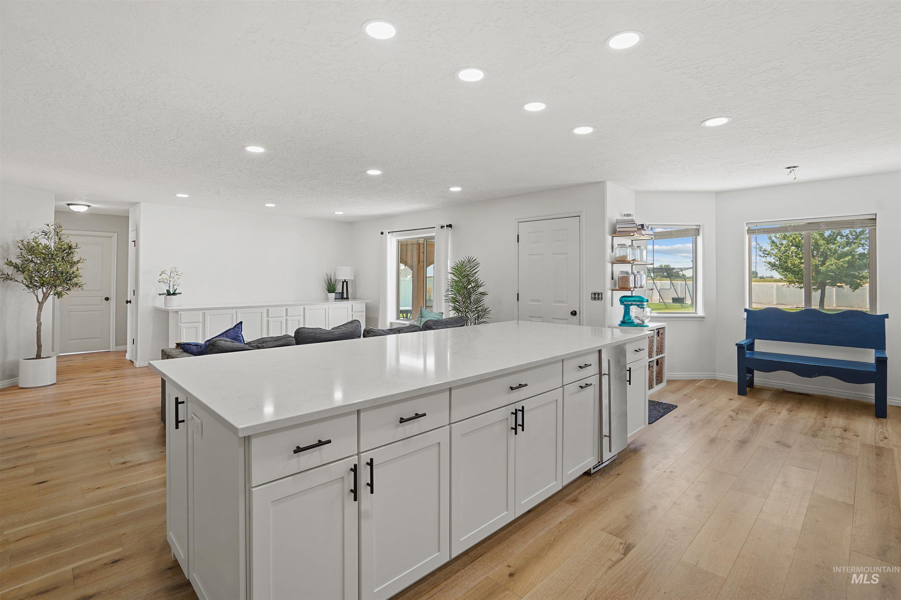 Kitchen featuring white cabinets, open floor plan, a textured ceiling, a kitchen island, and light wood-style floors