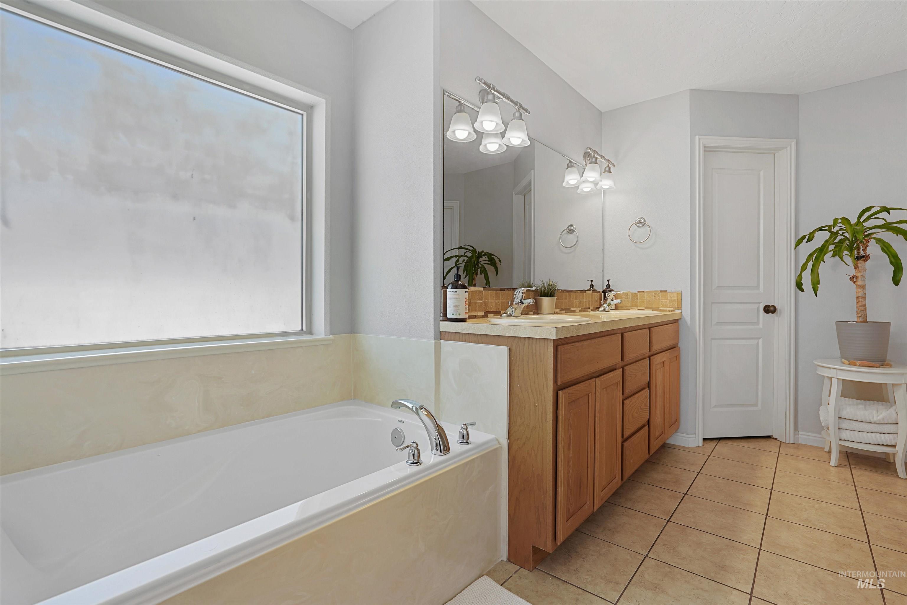 Bathroom with light tile patterned flooring, double vanity, and a bath