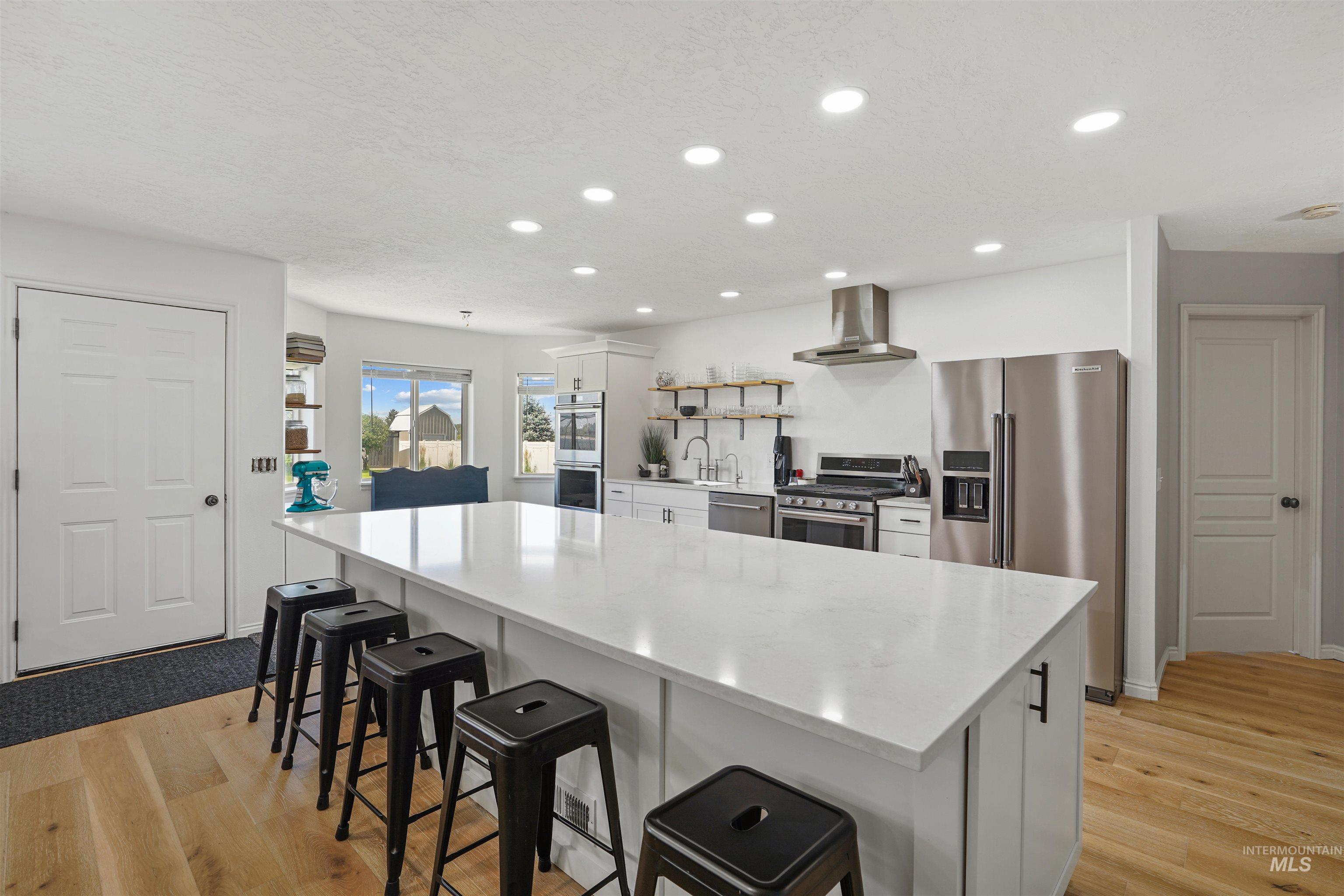 Kitchen with white cabinets, stainless steel appliances, a spacious island, open shelves, and light wood-style floors