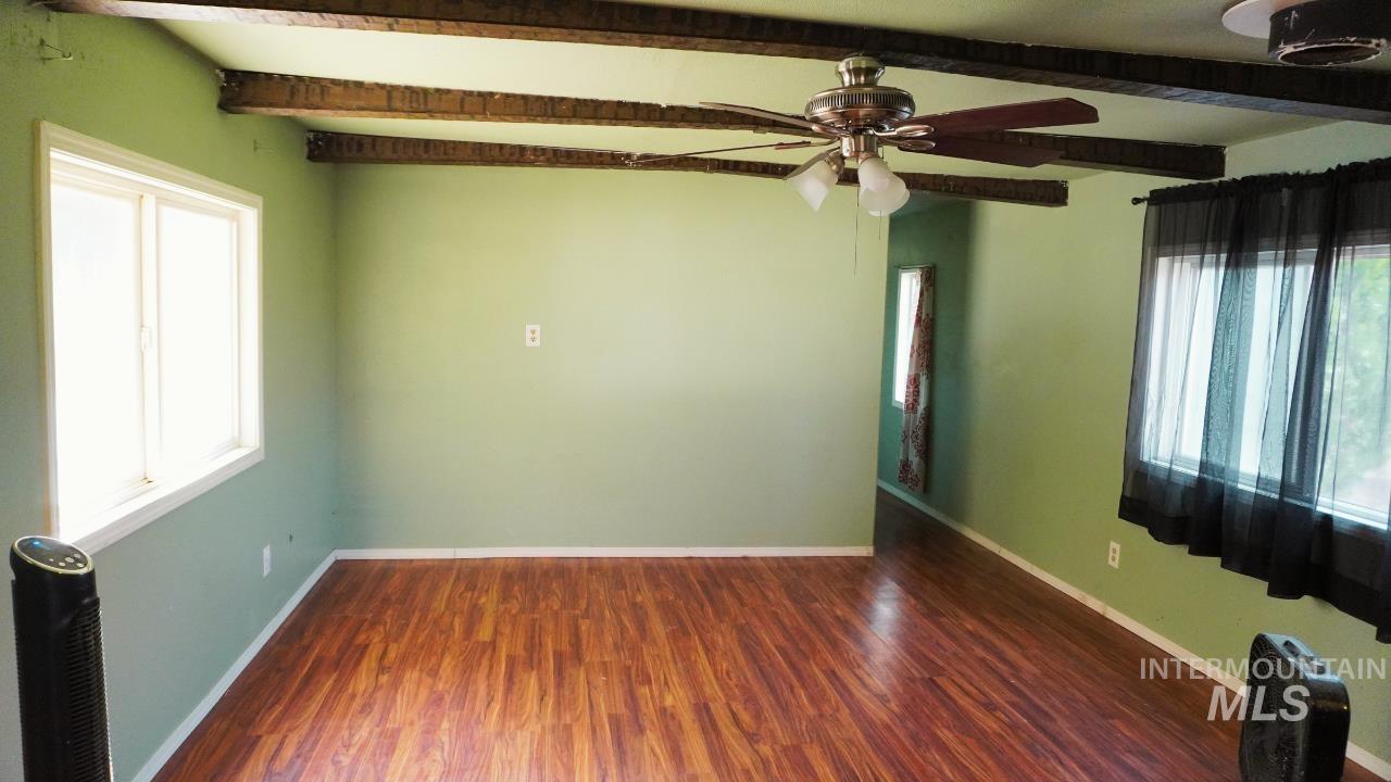 Spare room featuring dark wood-type flooring, beam ceiling, and a ceiling fan