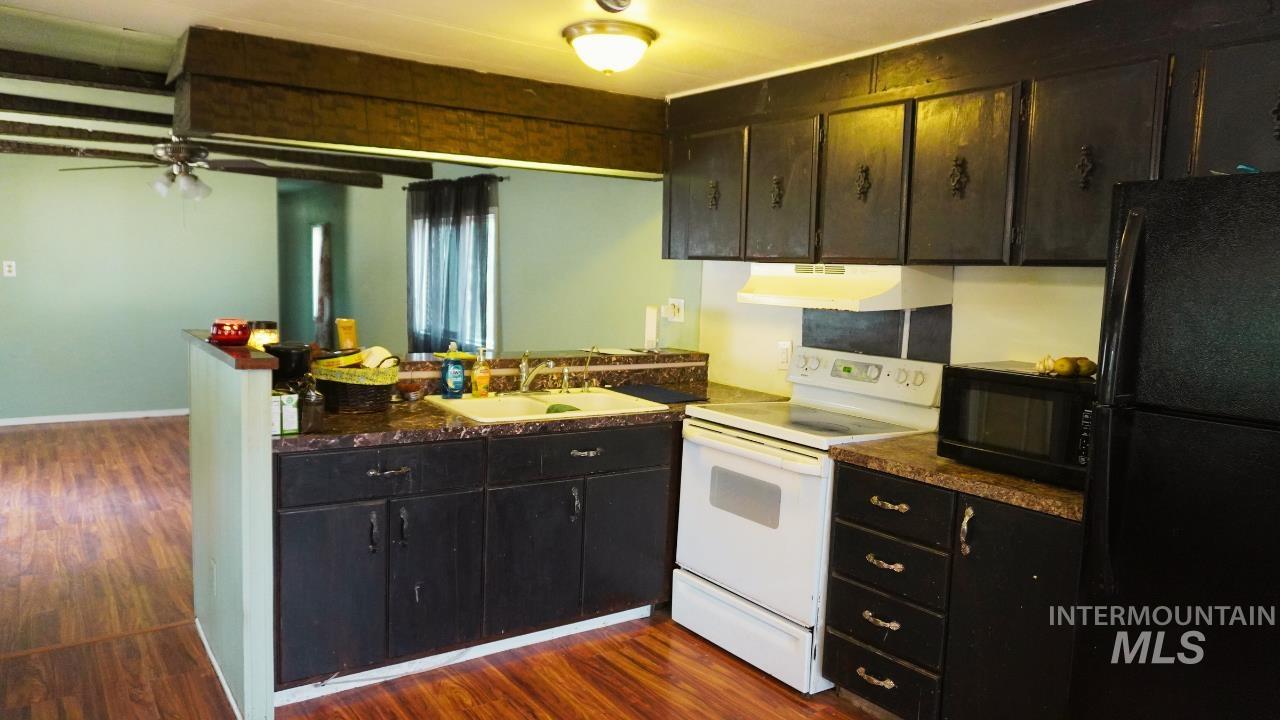 Kitchen featuring dark countertops, black appliances, a peninsula, and dark wood-style floors