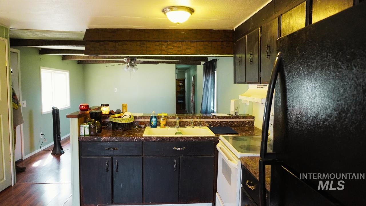 Kitchen with freestanding refrigerator, electric range, dark countertops, a peninsula, and under cabinet range hood