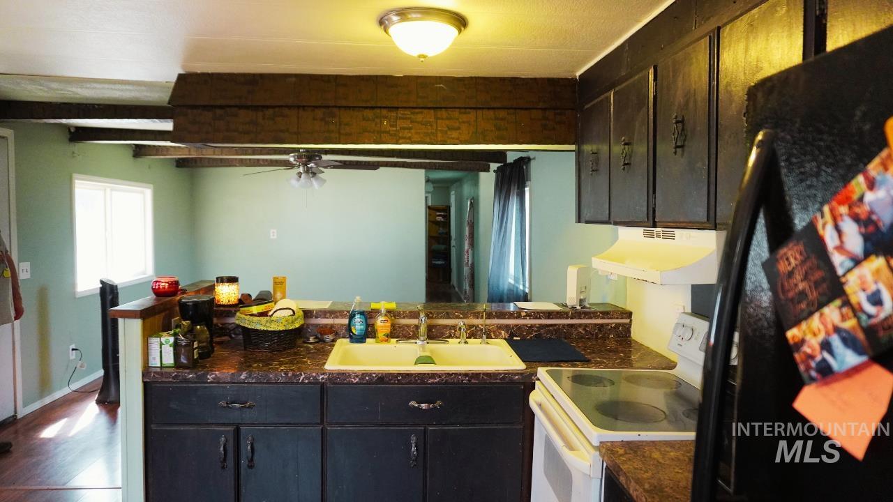 Kitchen featuring freestanding refrigerator, white range with electric cooktop, a peninsula, dark countertops, and under cabinet range hood