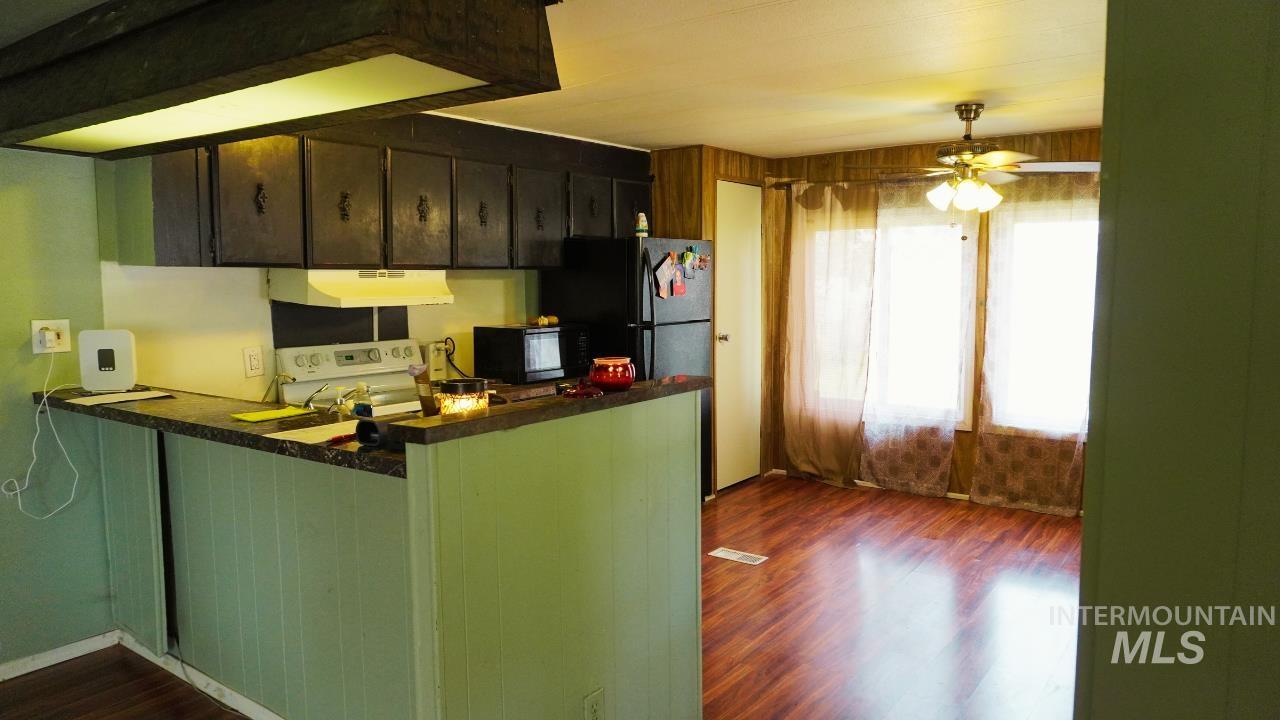 Kitchen featuring dark wood-style flooring, under cabinet range hood, black microwave, dark countertops, and white range oven