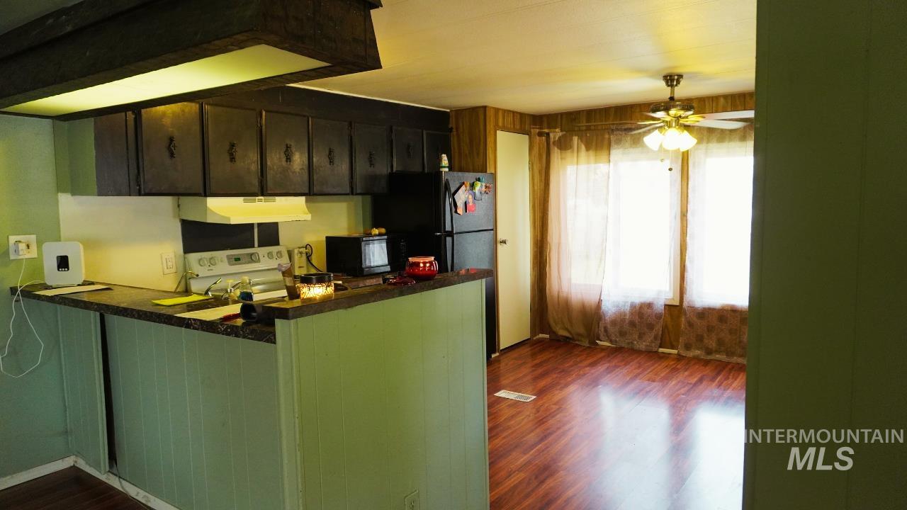 Kitchen featuring dark wood finished floors, white stove, black microwave, dark countertops, and ceiling fan