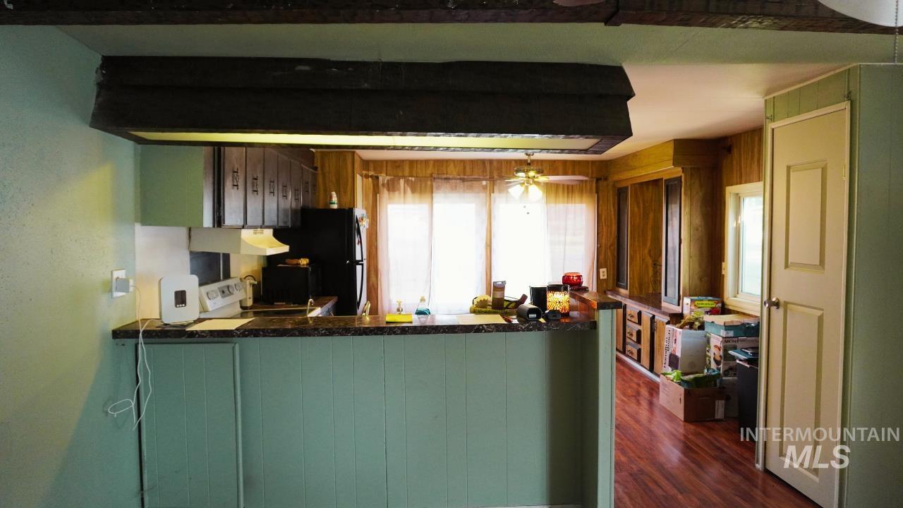 Kitchen featuring dark countertops, a peninsula, white stove, dark wood-type flooring, and under cabinet range hood
