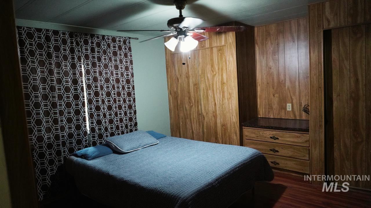 Bedroom featuring dark wood-style floors, wood walls, and ceiling fan