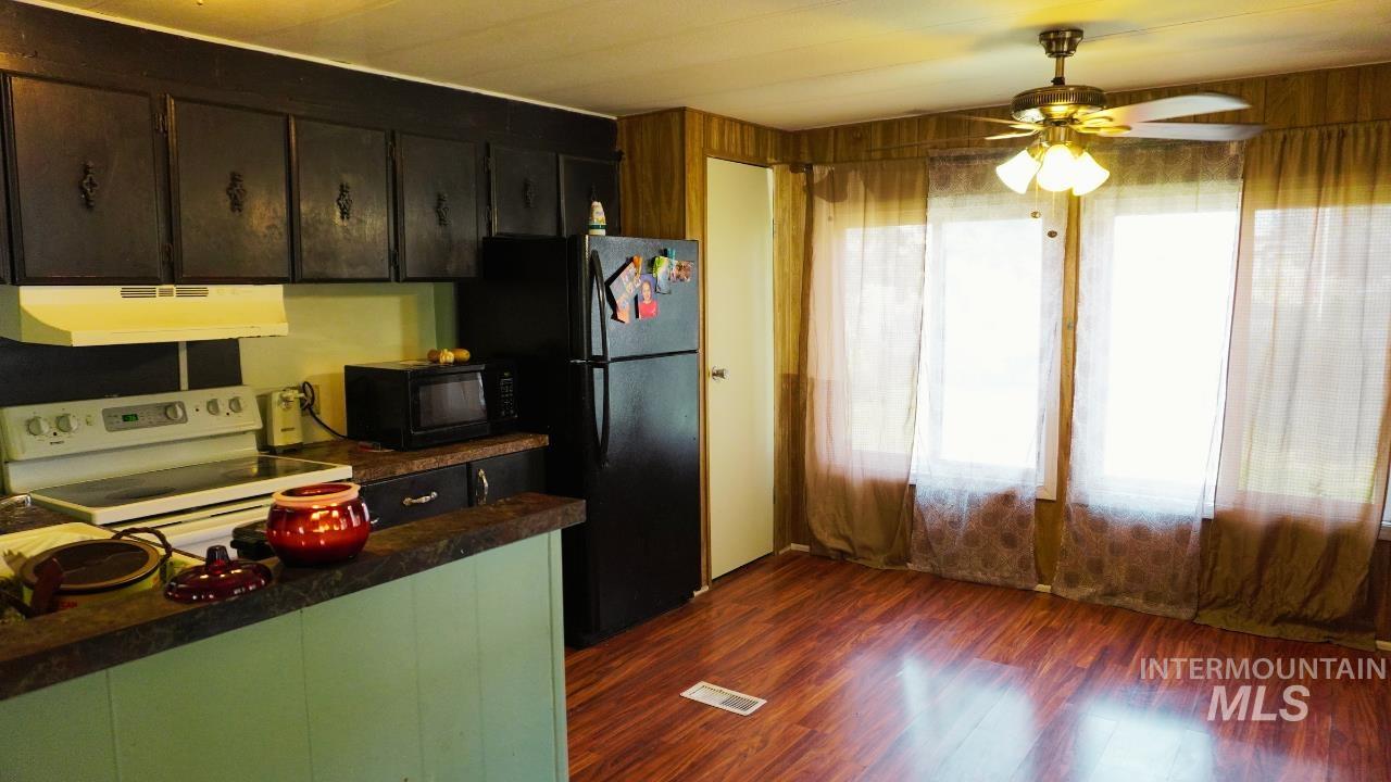 Kitchen featuring white range with electric stovetop, dark wood-style flooring, dark countertops, under cabinet range hood, and black microwave
