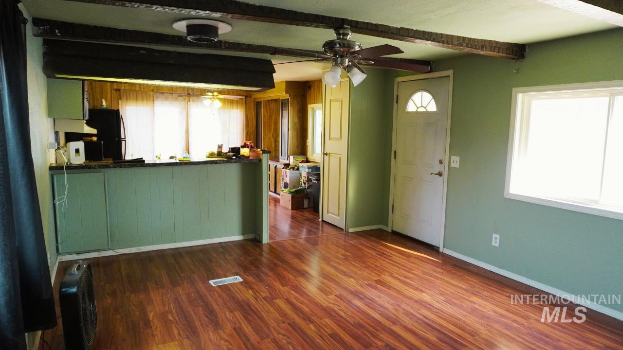 Unfurnished living room with dark wood-style flooring, plenty of natural light, beam ceiling, ceiling fan, and heating unit