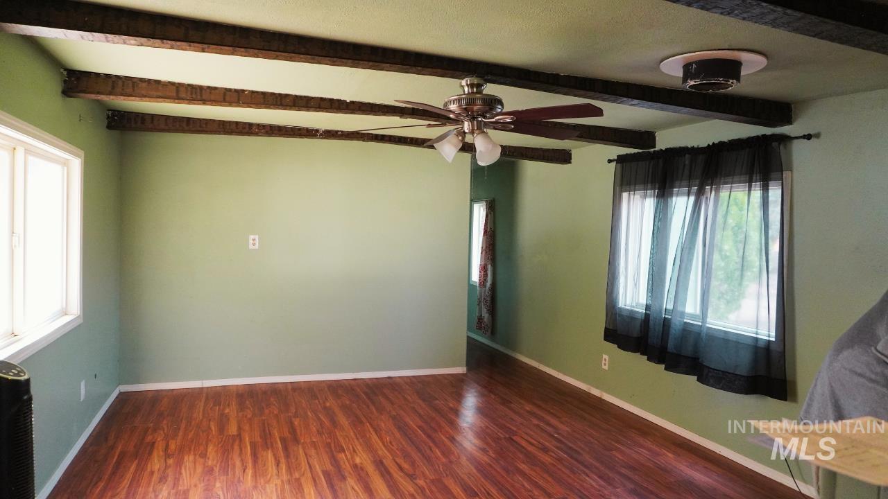 Unfurnished room featuring dark wood-style flooring, beamed ceiling, and ceiling fan