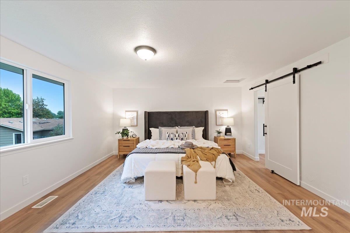 Bedroom featuring a barn door, light wood finished floors, and a textured ceiling