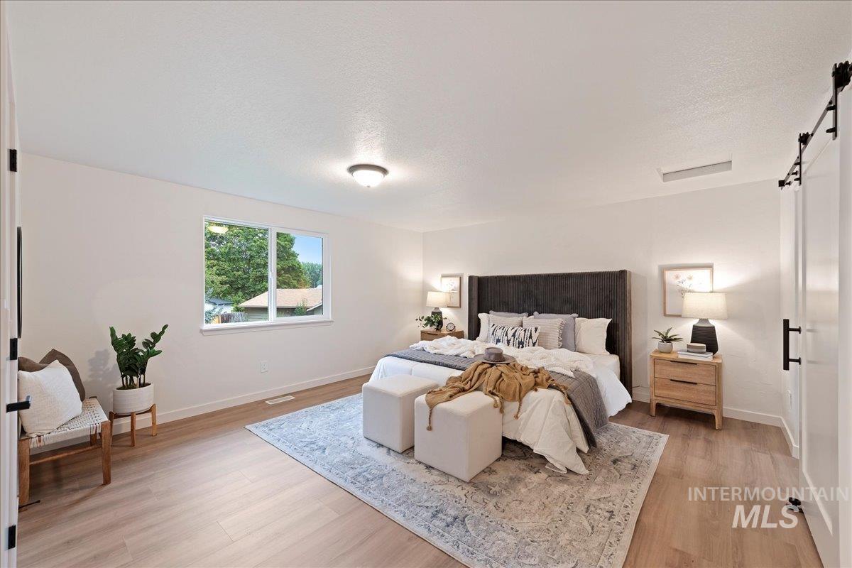 Bedroom featuring a barn door, light wood-type flooring, and a textured ceiling