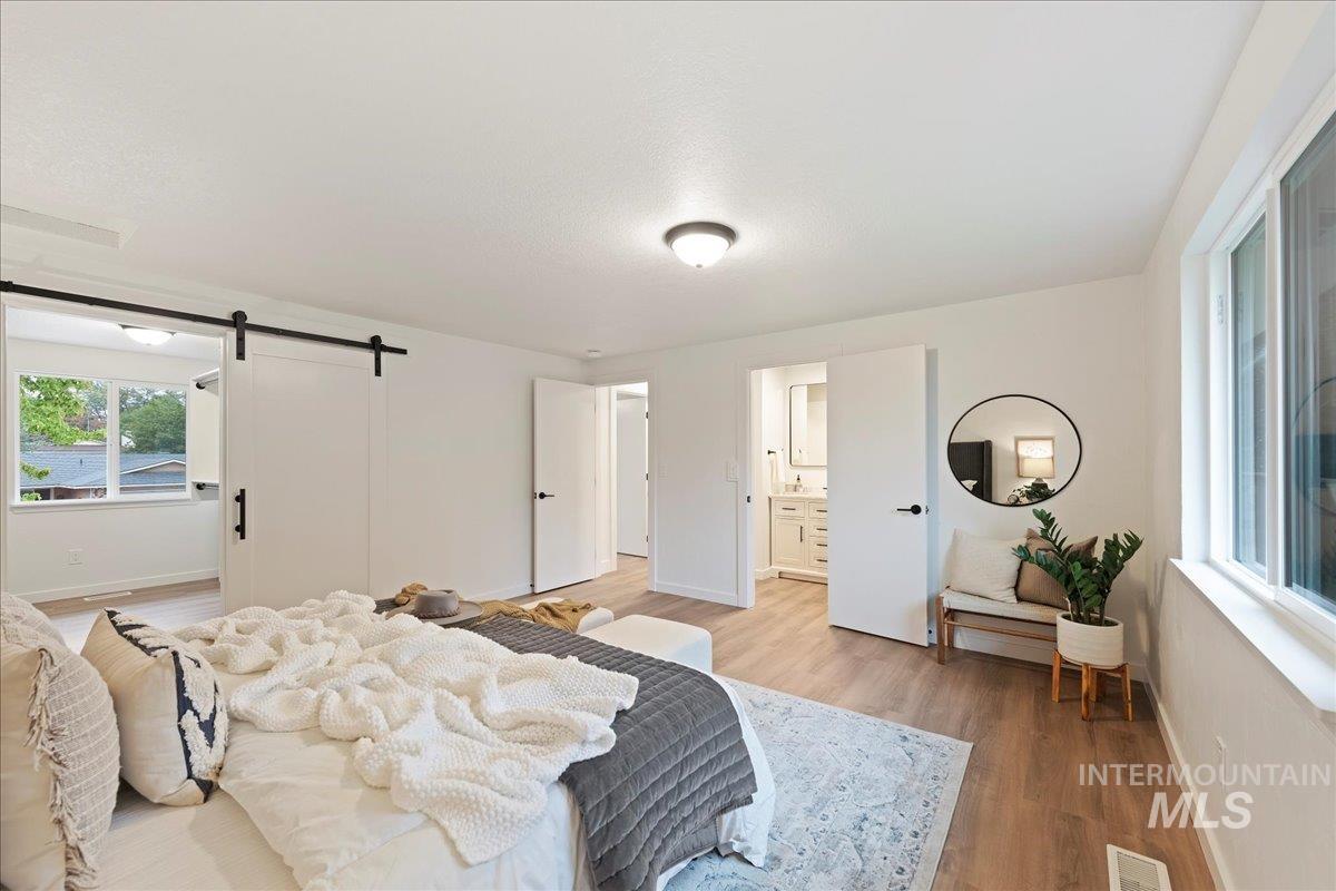Bedroom with ensuite bath, a barn door, and wood finished floors