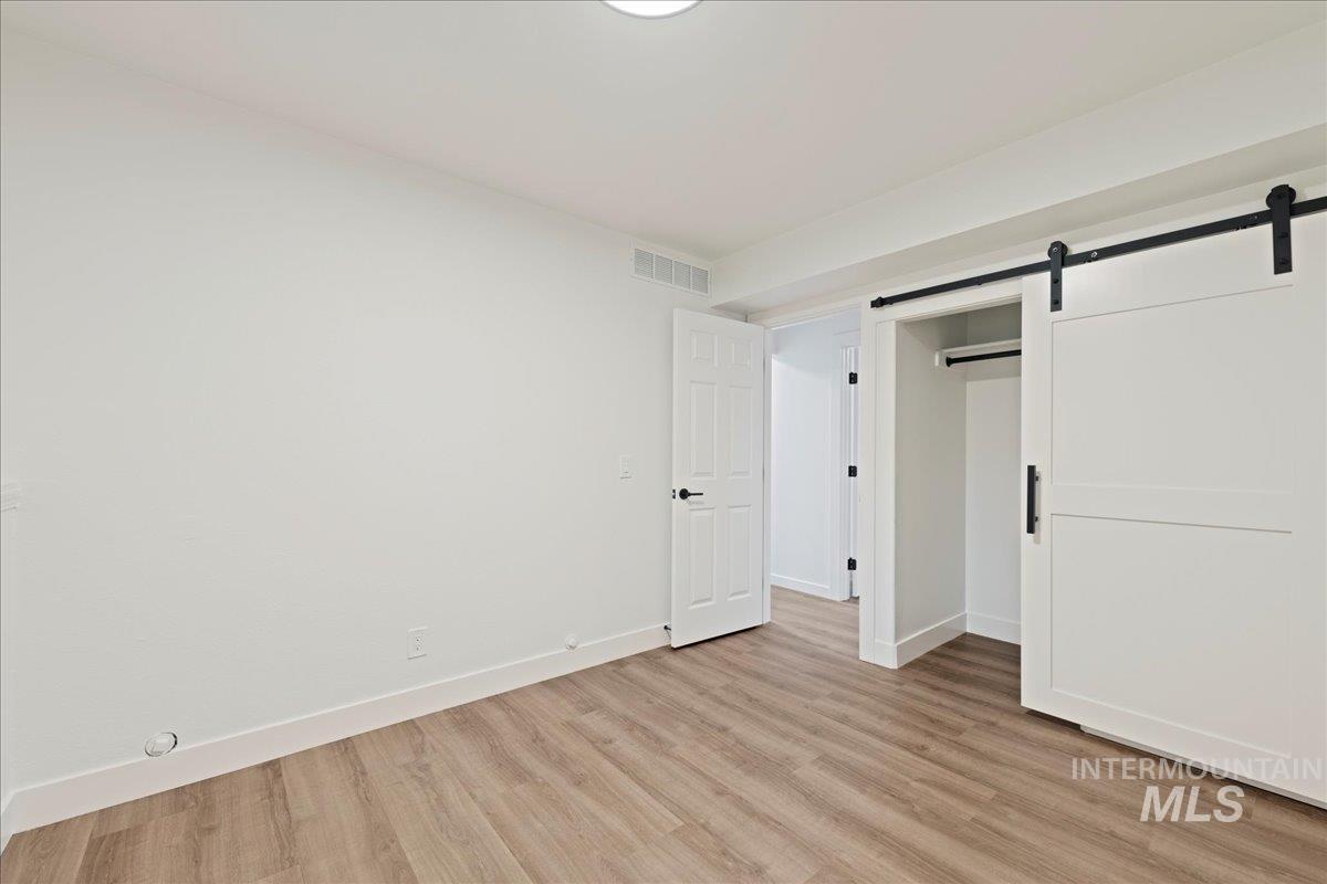 Unfurnished bedroom featuring a barn door and light wood-style flooring