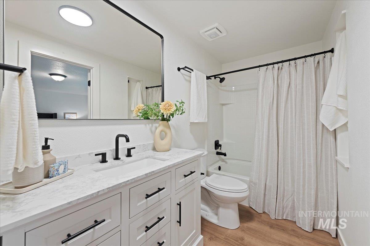 Full bathroom featuring light wood-type flooring, vanity, and shower / bath combination with curtain