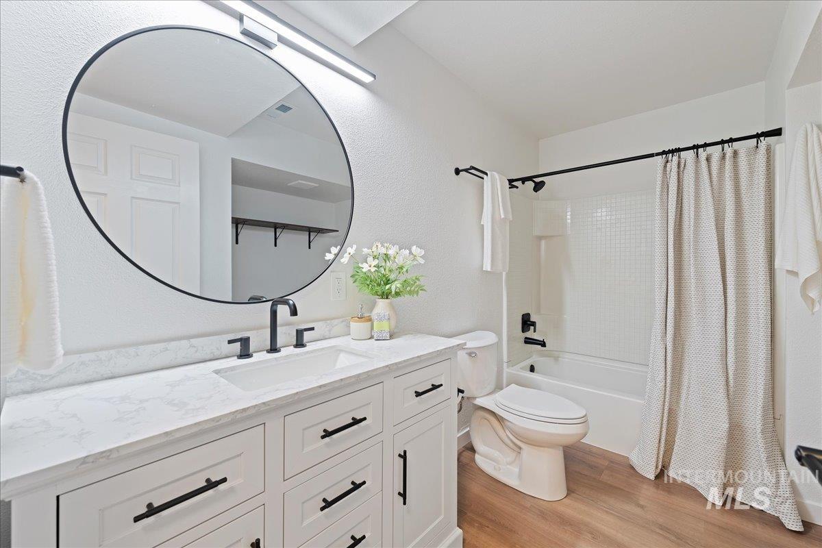 Full bathroom with light wood finished floors, shower / bath combo, vanity, and a textured wall