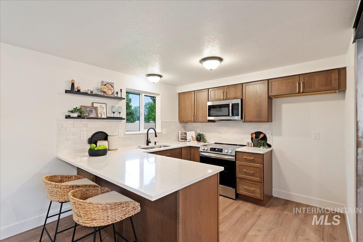 Kitchen featuring a peninsula, a breakfast bar area, backsplash, light wood-style floors, and a textured ceiling