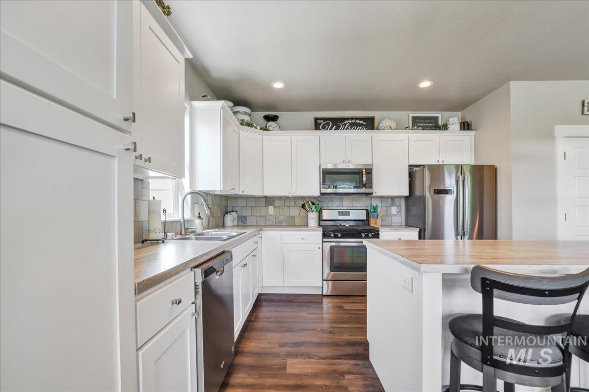 Kitchen with light countertops, stainless steel appliances, white cabinets, tasteful backsplash, and recessed lighting