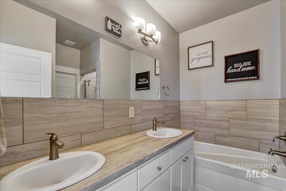 Bathroom featuring a bath, double vanity, and decorative backsplash