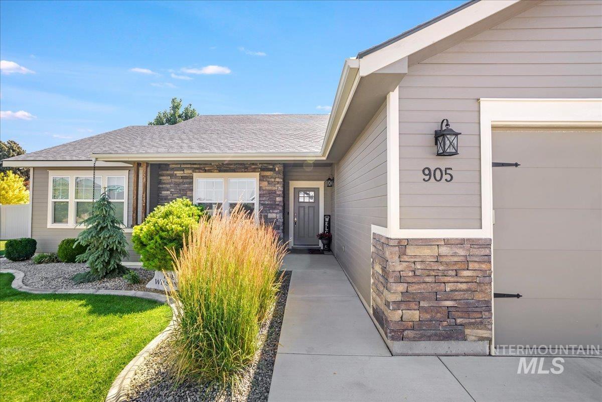 Entrance to property with stone siding, a garage, a shingled roof, and a lawn