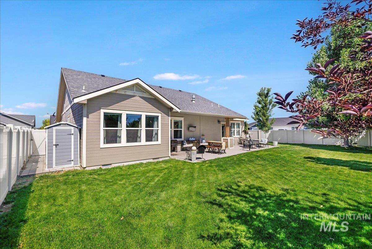 Rear view of house featuring a fenced backyard, a patio, a storage shed, and roof with shingles