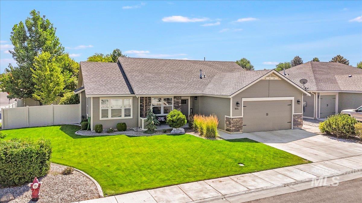 View of front facade featuring an attached garage, driveway, a shingled roof, and stone siding