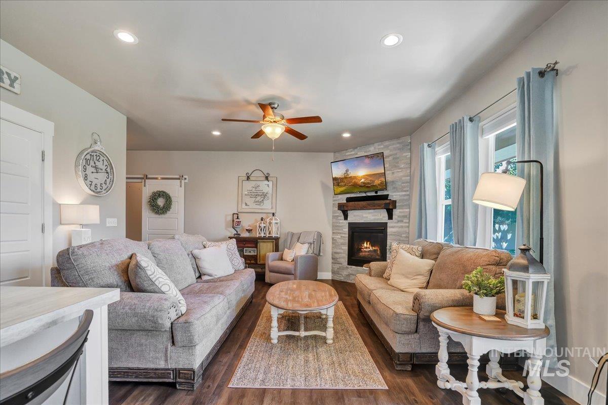 Living room featuring a barn door, dark wood-style floors, a ceiling fan, recessed lighting, and a stone fireplace