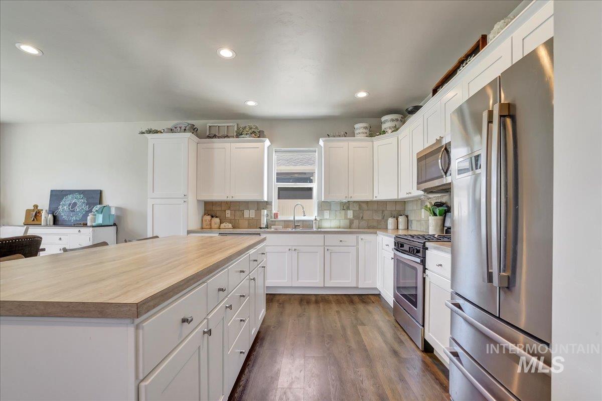 Kitchen featuring stainless steel appliances, decorative backsplash, white cabinets, and recessed lighting