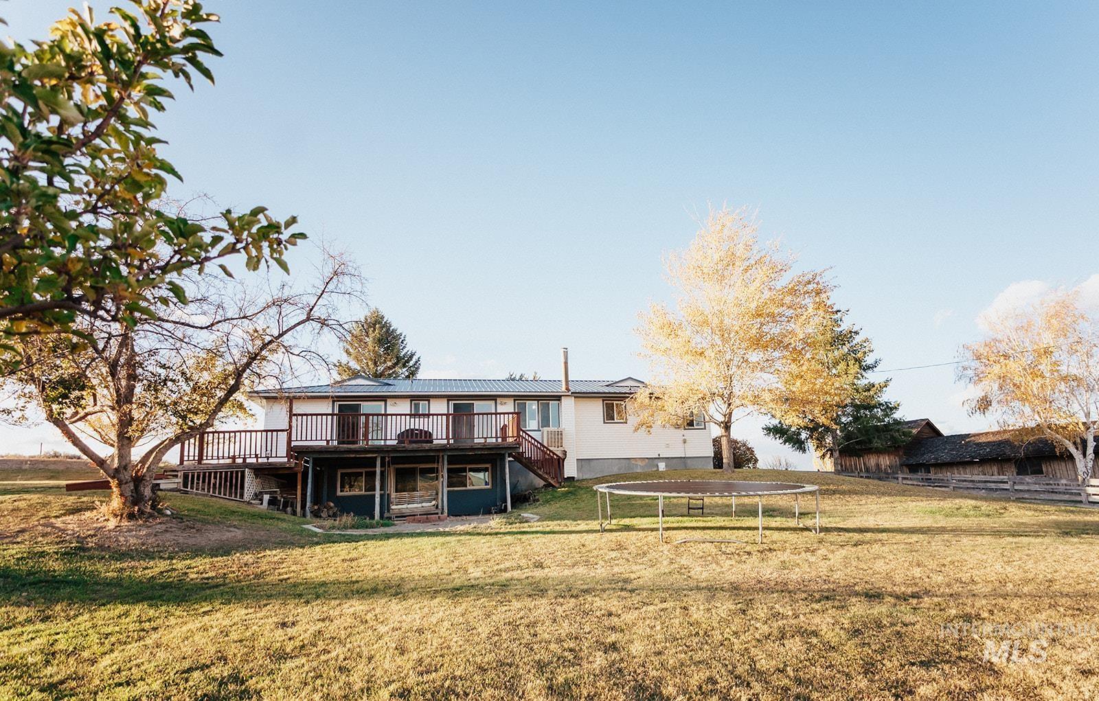 Back of property with a trampoline, a lawn, a deck, and stairs