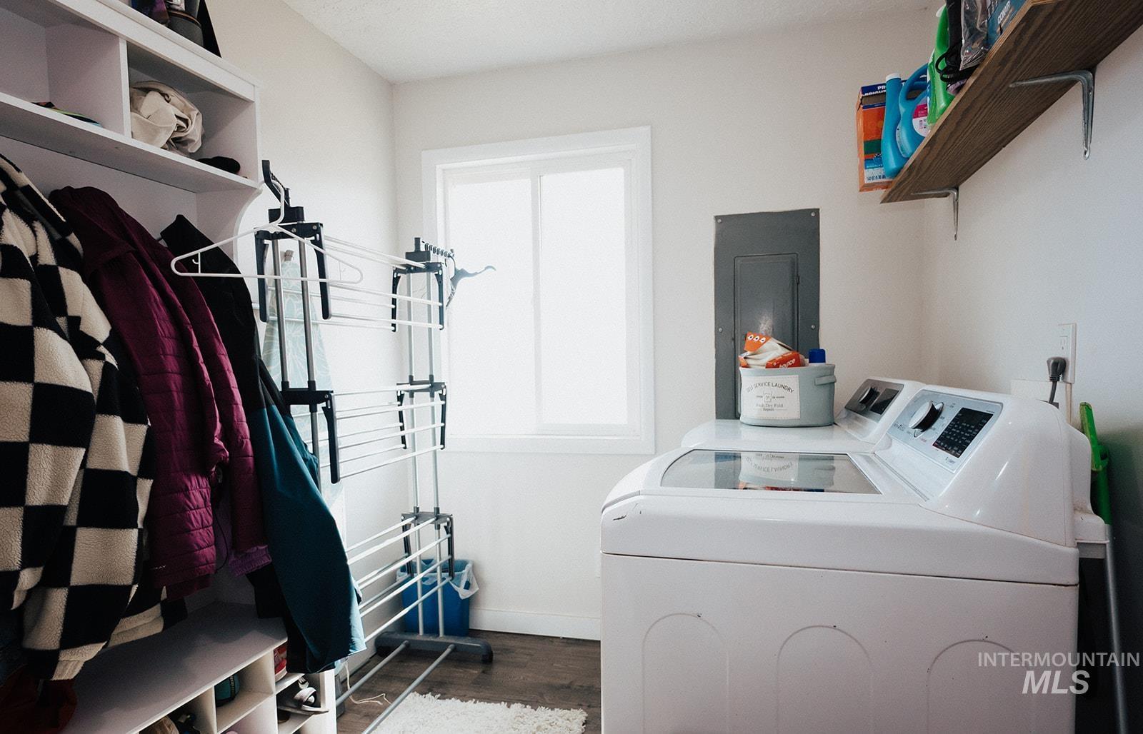 Washroom with dark wood-style floors, washer and clothes dryer, and electric panel