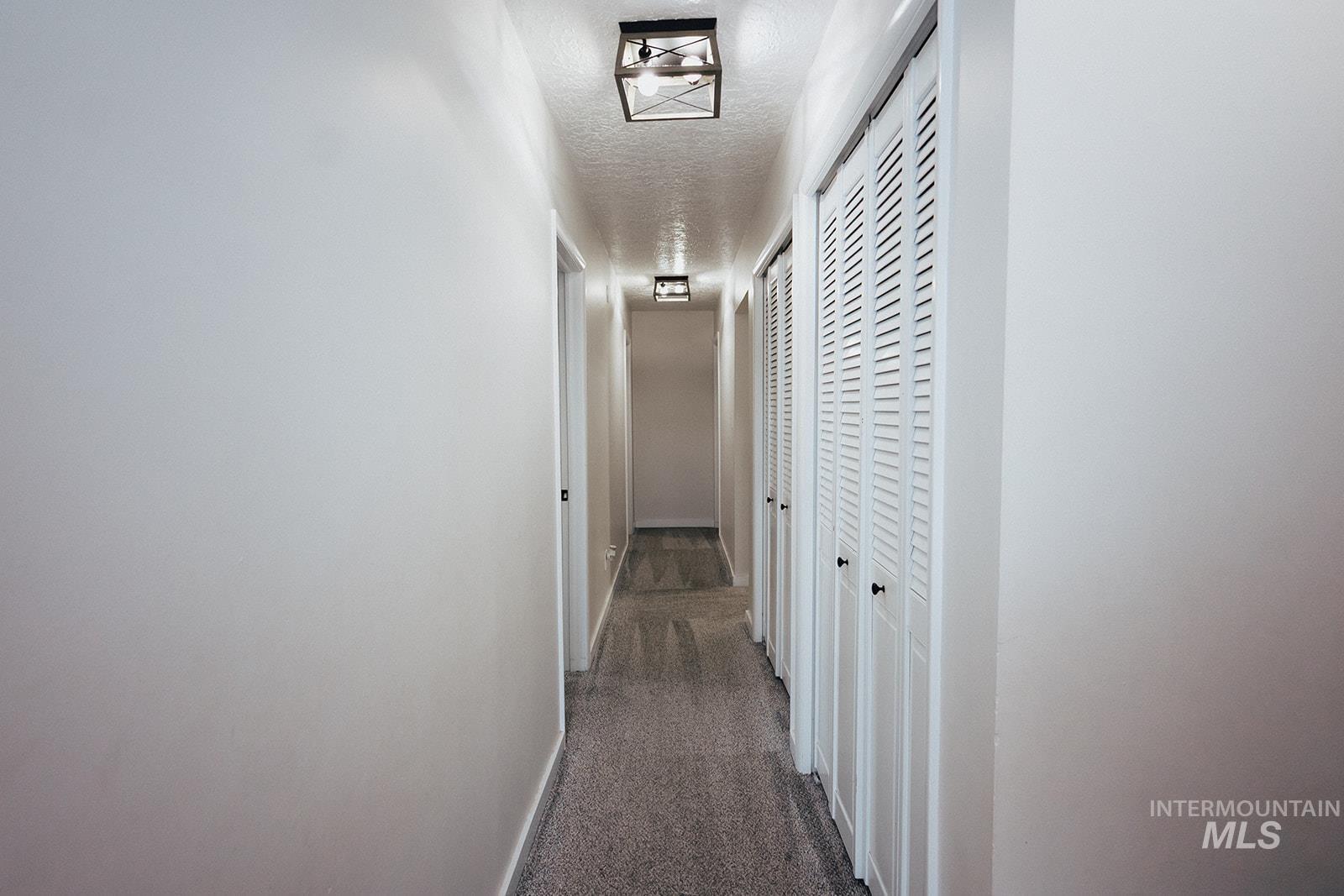 Hallway featuring dark colored carpet and a textured ceiling