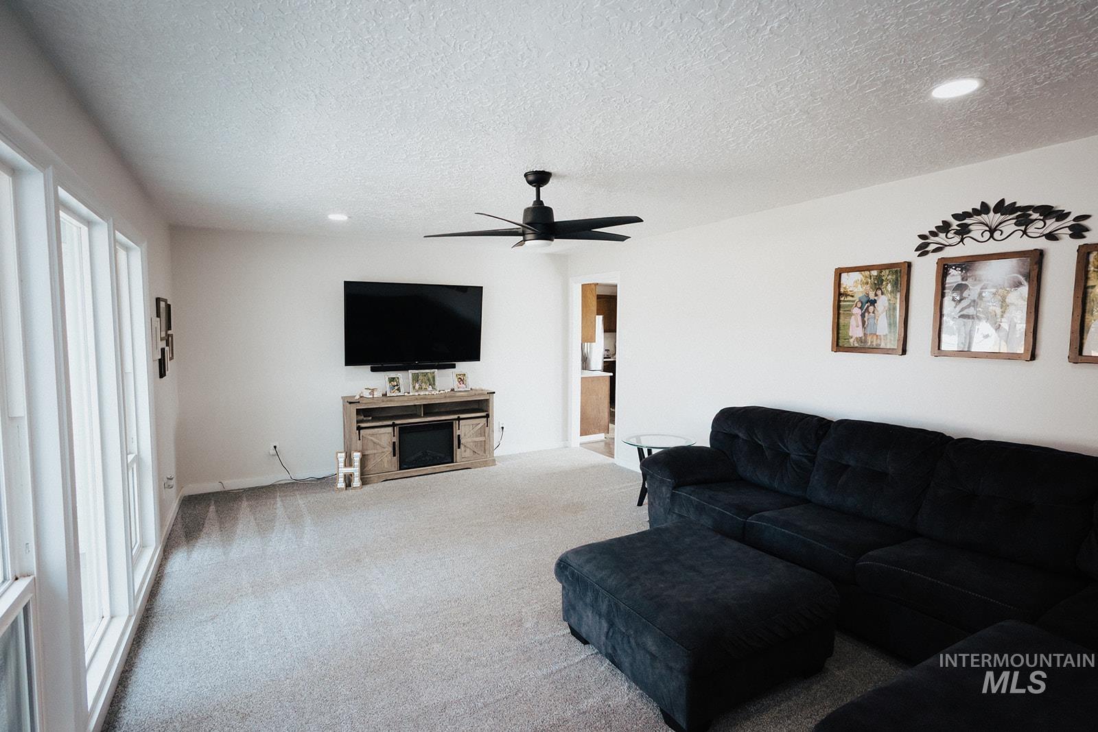 Living room with carpet, a textured ceiling, a ceiling fan, a fireplace, and recessed lighting